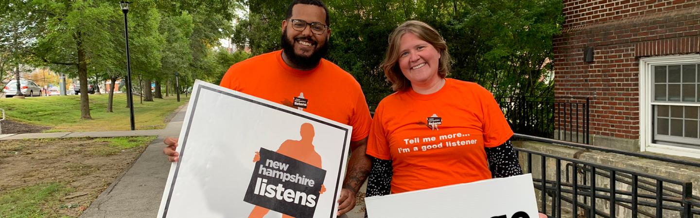 Carrie and Andres holding NH Listens signs in front of Huddleston Hall.