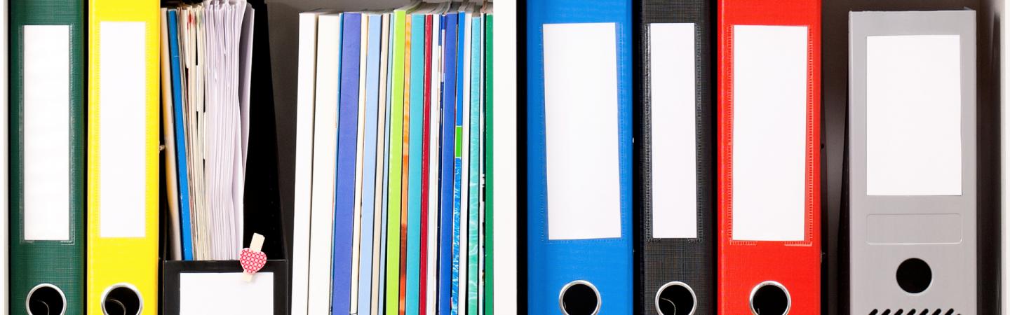 A photo showing multicolored binders and magazines organized on a shelf