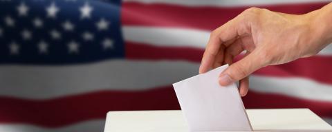 person placing ballot in voting box with american flag in background