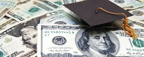 Photo of graduation cap on stacks of money.
