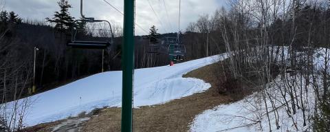New hampshire ski area in winter with patches of exposed ground alongside snow covered trails and chair lift. Photo by Maddie Smith. 