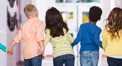 back view of elementary school students holding hands and walking down hallway
