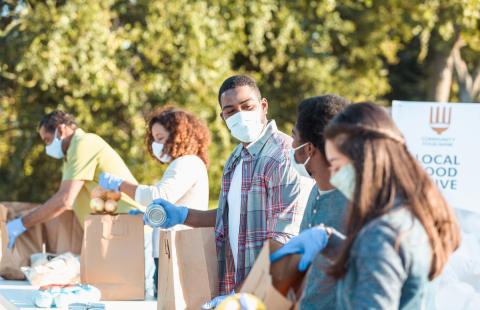 A group of nonprofit workers wearing masks and filling paper bags during a local food drive