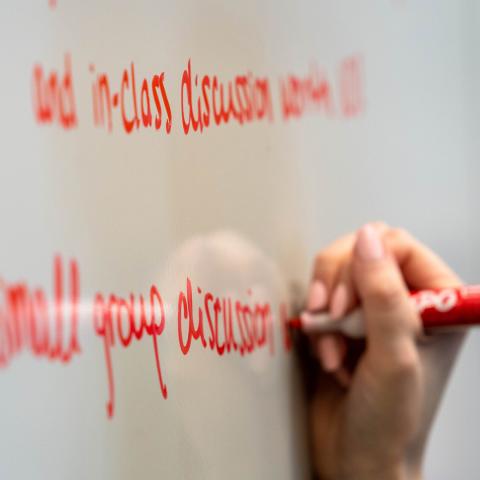 Image of a woman's hand writing red text on a white board.