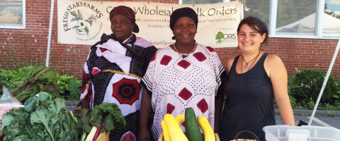 MCD graduate Charlene Higgins (far right) standing with two farmers at a produce stand.