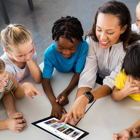 children sitting around a table looking at a tablet