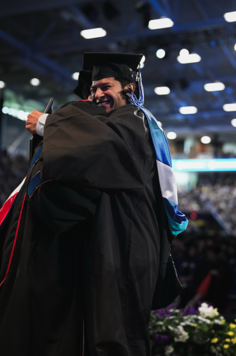 public policy alum Thomas Galarneau receiving his diploma on stage at commencement and hugging Director Stephen Bird