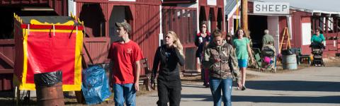 three young adults  in foreground walking at NH fair with farm buildings in background
