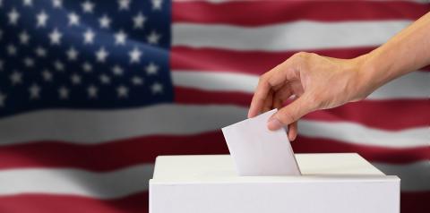 person casting vote in voting box with american flag in background