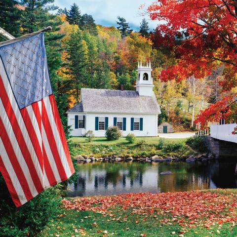 A photograph of a new hampshire church in the fall with an American flag hanging in the forefront