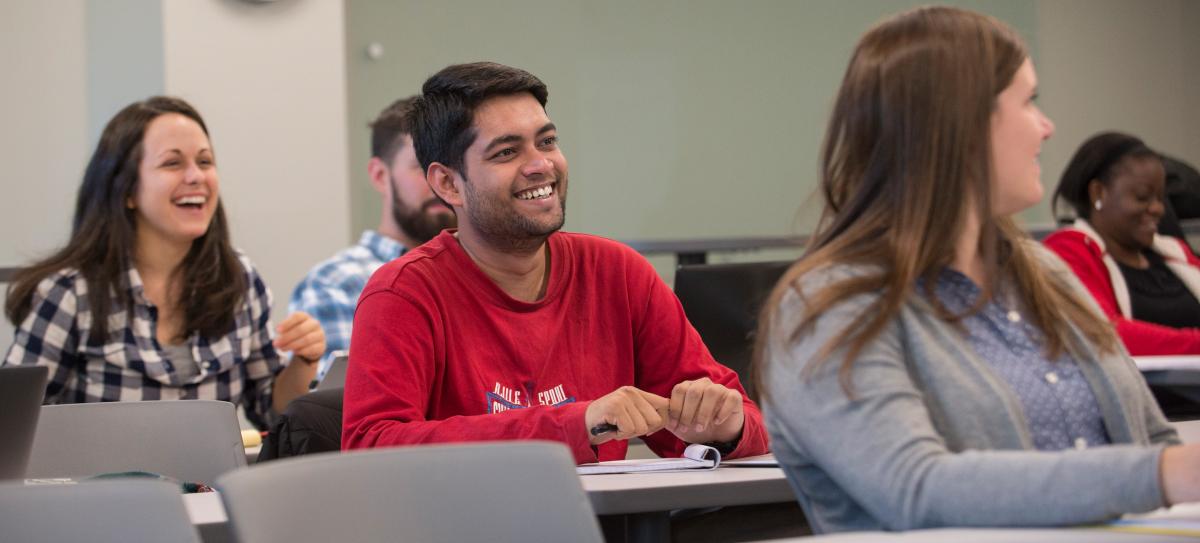 Two students sitting in a public policy classroom, listening to a lecture while smiling.