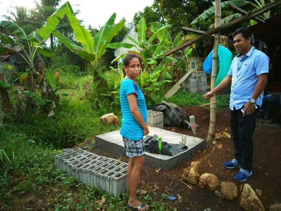 A man and a women standing near palm trees, next to a sewage treatment structure.